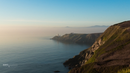 The lighthouse in the foggy distance. The red of the sunset is still seen in the fog.